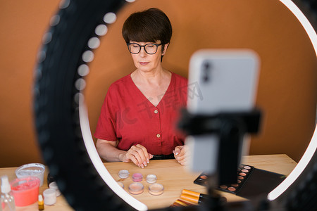 中年妇女在录制视频时用眼影、腮红调色板和刷子谈论化妆品。