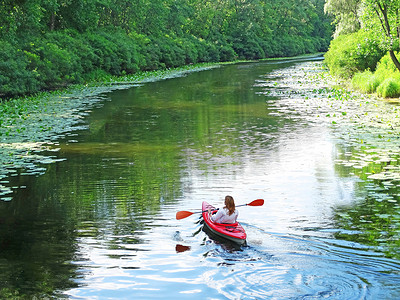一个女孩梦幻般地将她的皮划艇漂流到河上，周围环绕着河流植物。