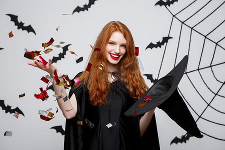 万圣节女巫概念-快乐优雅的女巫投掷五彩纸屑，庆祝蝙蝠和蜘蛛背景下的万圣节派对。