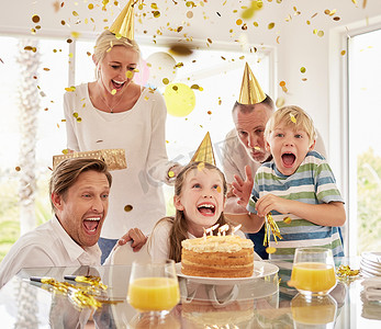 派对banner摄影照片_欢快的世代幸福家庭戴着派对帽，在家里用五彩纸屑和蛋糕庆祝小女孩的生日。