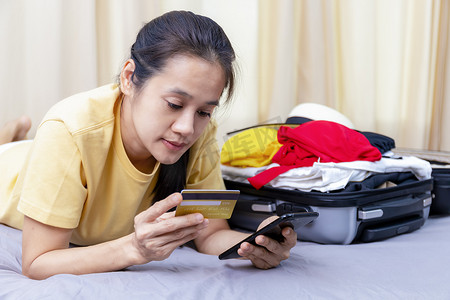 亚洲快乐的女人计划在家里的床上用手机和信用卡旅行。