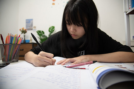 亚洲女学生正在书桌上写作业和看书