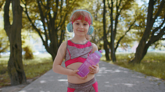 戴着耳机听最喜欢的音乐歌曲拿着水瓶的健身运动跑步小女孩
