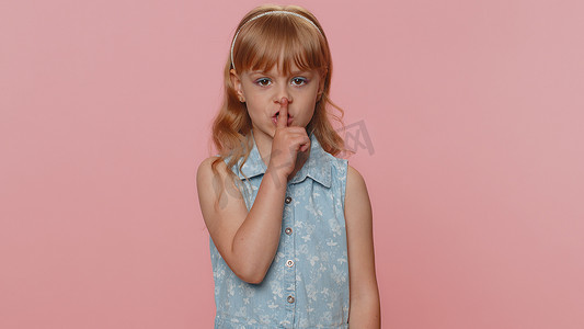 八卦摄影照片_青春期前的小女孩将手指按在嘴唇上，保持安静，安静标志不要说出八卦秘密，安静