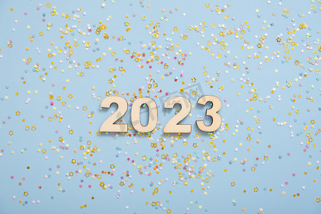 柔和的蓝色背景上的木制数字 2023，带有星星。