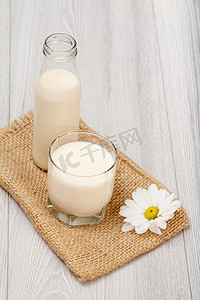 灰色木质背景中的一瓶和一杯牛奶、雏菊花