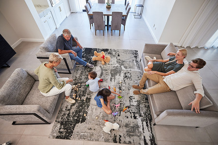 客厅里的大家庭与父母、婴儿或孩子一起在地毯上玩耍，以促进成长、发展和健康。