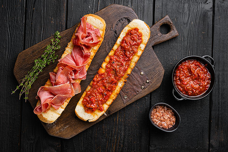硬皮烤面包配新鲜西红柿和腌制火腿，以黑色木桌为背景，俯视平躺