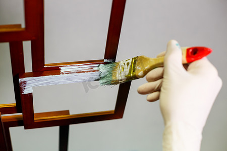 大师用刷子在木制棕色相框上涂上浅色油漆