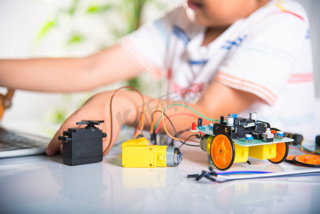编程教育摄影照片_亚洲男孩用笔记本电脑为 Arduino 机器人汽车学习编码和编程