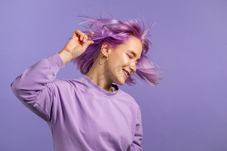 有魅力的女人，有着紫色的发型，在紫色工作室的背景下跳舞，她的头发在气流中飘扬。