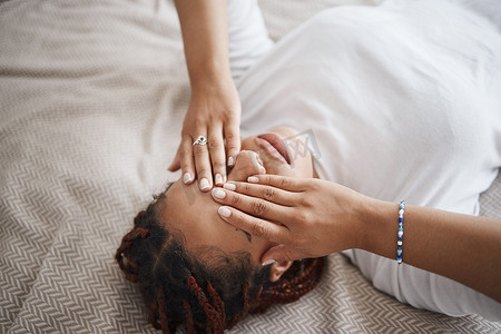 失眠和疲惫的黑人妇女在卧室的床上放松，一边遮住眼睛一边思考。