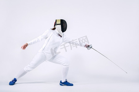 面具脸摄影照片_年轻的击剑运动员戴着面具和白色击剑服装。