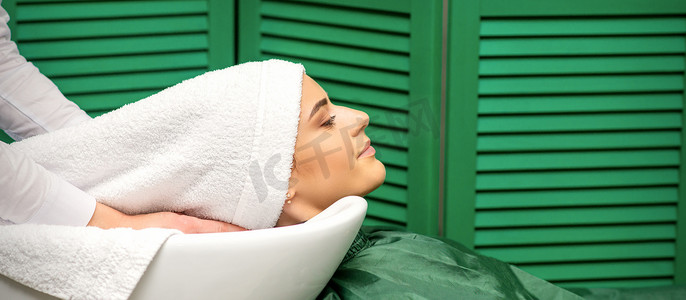 美发沙龙摄影照片_一位年轻白人女子在美发沙龙洗头后，理发师用白毛巾包裹头发。