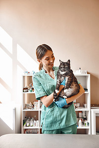 你害怕吗？可爱的年轻女兽医站在兽医诊所，抱着一只大黑猫，微笑着看着他