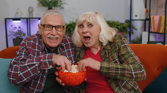 电视足球摄影照片_高级家庭夫妇祖父母男女看有趣的电视足球电影，吃爆米花
