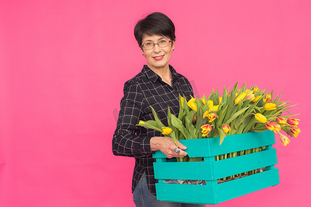 粉红色背景中拿着蓝色郁金香木盒的中年女卖花人