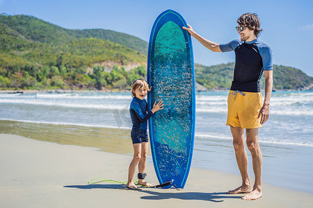 海上冲浪运动摄影照片_父亲或教练教他的儿子如何在假期或假期在海上冲浪。
