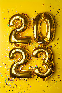2023喜庆摄影照片_2023 年概念新年快乐从金箔气球和黄色背景的五彩纸屑