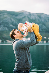 微笑的爸爸在水的背景下将婴儿举过头顶