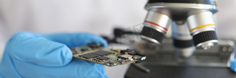 微电路摄影照片_手套的工程师在显微镜背景下拿着微电路