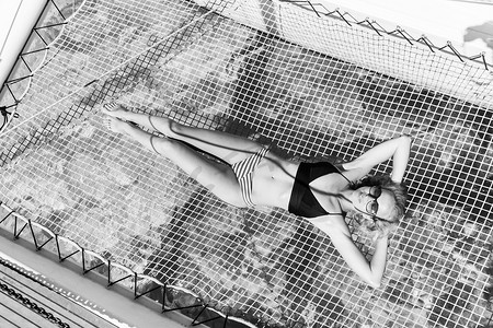 女人穿着比基尼晒黑，在夏季帆船巡游中放松，躺在豪华双体船的吊床上。