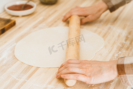 鳞片摄影照片_不露面的女人在家里的餐桌上用擀面杖擀面团，