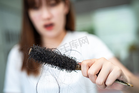 亚洲女性有长脱发问题，头发附着在梳子上。