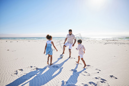 无忧无虑的父亲和两个孩子在海滩上踢足球。