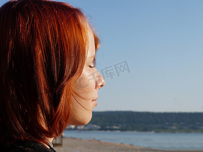 一个红发少女的侧影，闭着眼睛，特写在大海的背景下，复制空间