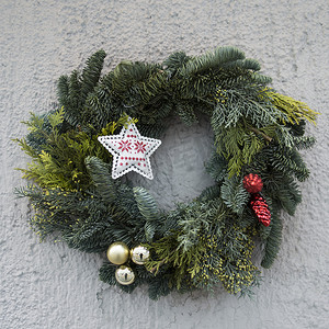 星星挂饰摄影照片_冷杉树枝的圣诞花环，房子的灰色墙上挂着装饰、星星、球