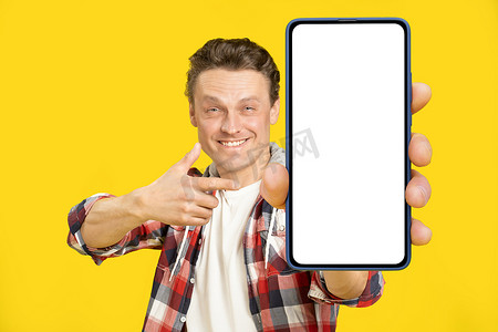 指着巨大的智能手机，上面有白色空屏幕的金发男子，身穿红色格子衬衫。