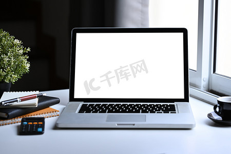 白色办公桌上的前视图样机笔记本电脑、咖啡杯、笔记本和计算器。