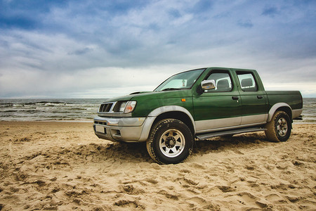绿色皮卡车停在沙滩上，背景是大海、蓝天和云彩