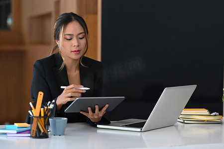 有魅力的女性经济学家使用数字平板电脑并在办公室处理会计文件。