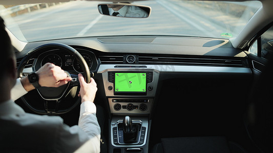 五一幕布摄影照片_穿着白衬衫的经典休闲商人在驾驶一辆带有绿屏模型显示仪表板服务菜单应用程序的汽车时手上使用智能手表的后视图。