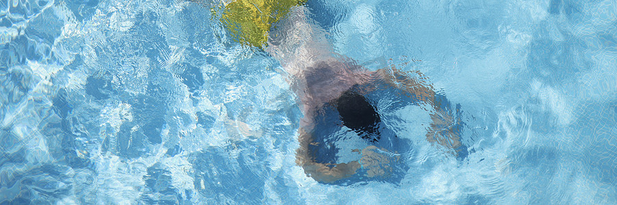 游泳池里的男性在腹部漂浮在水面上，在深度潜水