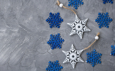 圣诞树上的两个白色装饰品以雪花和许多蓝色雪花的形式躺在灰色的混凝土背景上。