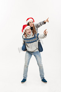 圣诞节概念 — 身穿毛衣的年轻幸福夫妇享受白色灰色背景中的背驮式骑行
