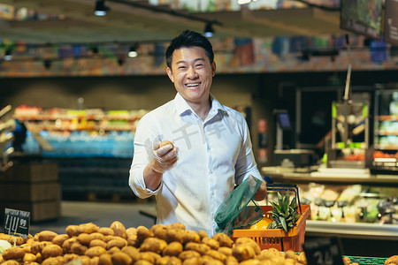 水果商店摄影照片_一个亚洲男人站在蔬菜区的一家超市里，手里拿着土豆
