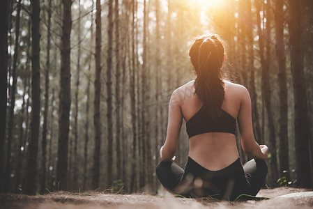 美丽的女人在宁静的天然森林里做瑜伽姿势的后视图。