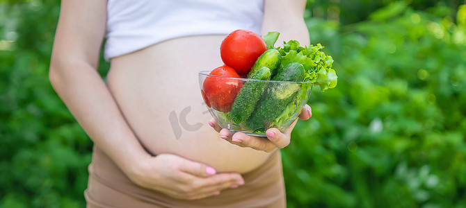 一名孕妇手里拿着蔬菜。