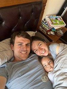 父亲封面摄影照片_微笑的妈妈、爸爸和小女儿躺在床上的被子下