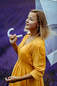 紫色花伞摄影照片_雨天，薰衣草田里的中年妇女打着伞散步，享受香薰。