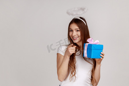 带着光环的天使般的女人拿着礼品盒，指着相机，选择获胜者送礼物。
