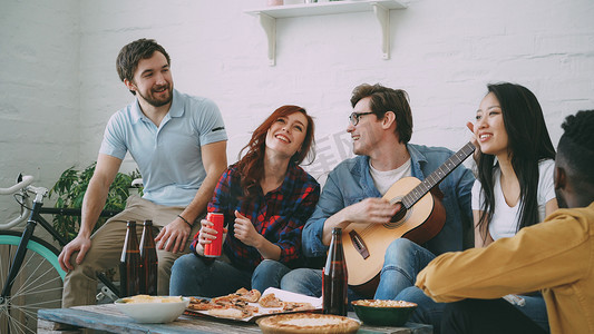 快乐的年轻朋友在合租公寓举办派对，一起唱歌，而他们的朋友在家里弹吉他