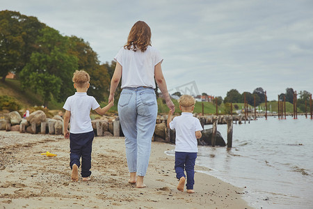 孩子散步摄影照片_年轻的母亲带着她的儿子在海滩上散步