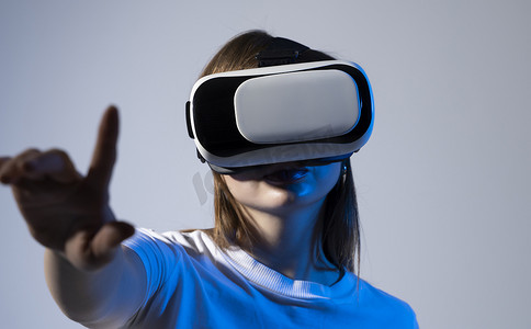 戴着ar摄影照片_身着白色 T 恤、戴着虚拟现实耳机的黑发年轻女子在 Metaverse 虚拟现实体验中触摸空气。