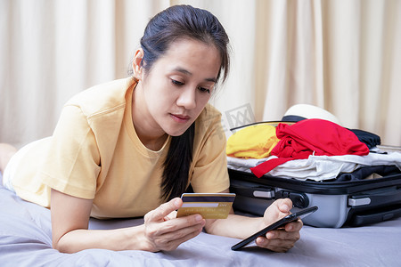 亚洲快乐的女人计划在家里的床上用手机和信用卡旅行。