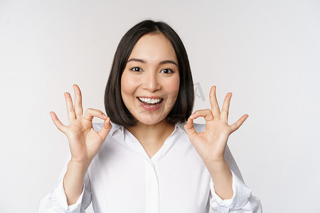 推荐摄影照片_特写亚洲女孩的头像，表现出好的、好的手势和满意的微笑、推荐、高兴、赞美和恭维，白色背景